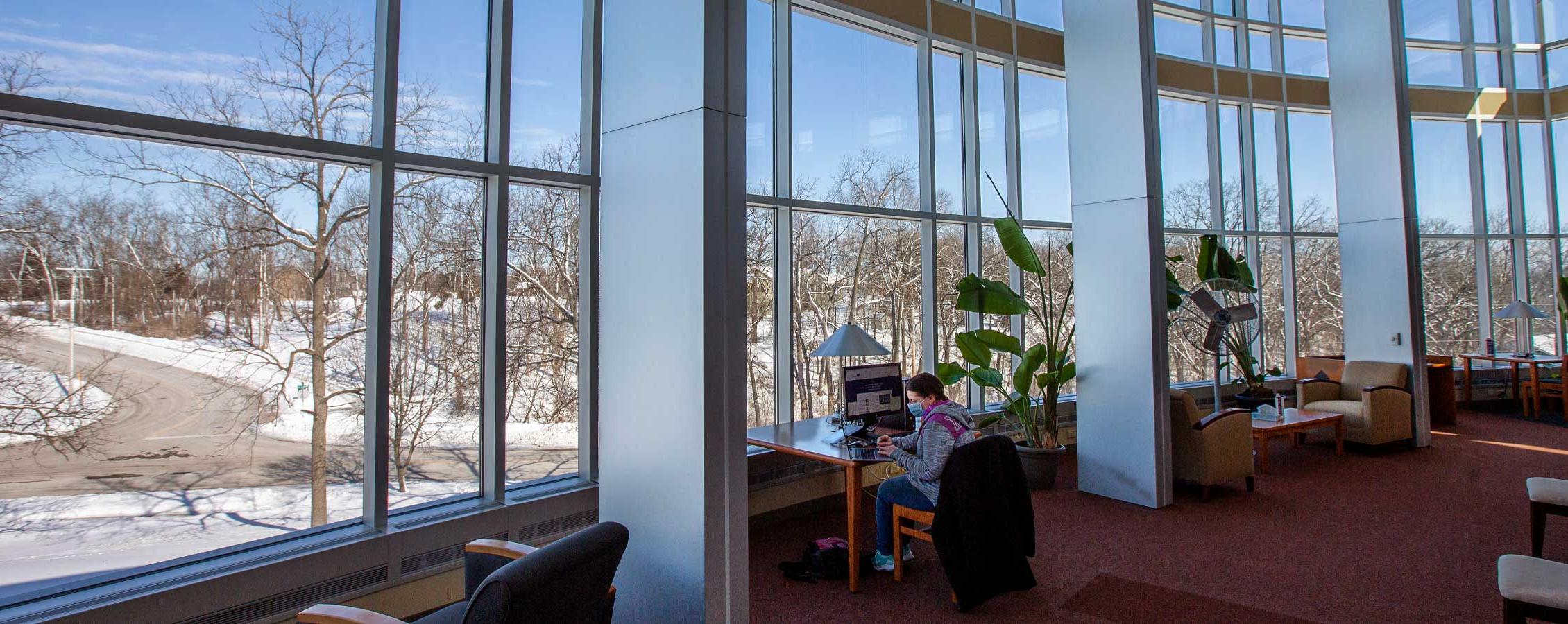 A student sits in front of the large windows in the Lenox Library on the 足彩平台 Rock County campus.