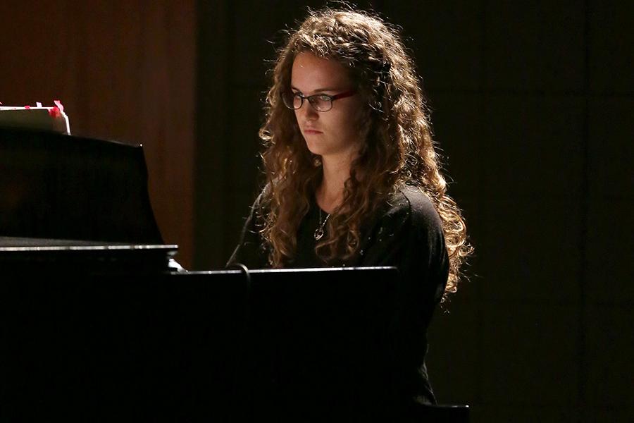 A person wearing a black shirt plays a black piano.