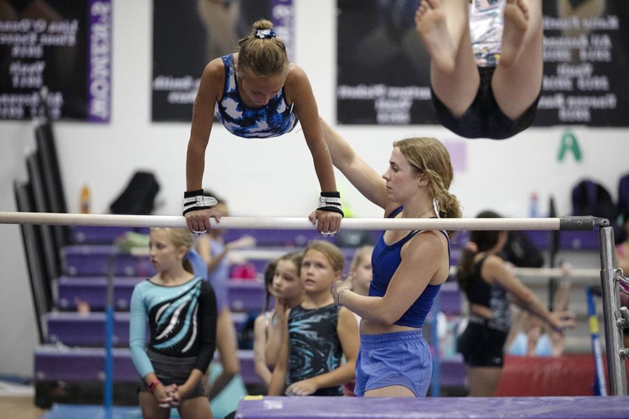 A person helps another person over a gymnastic bar.