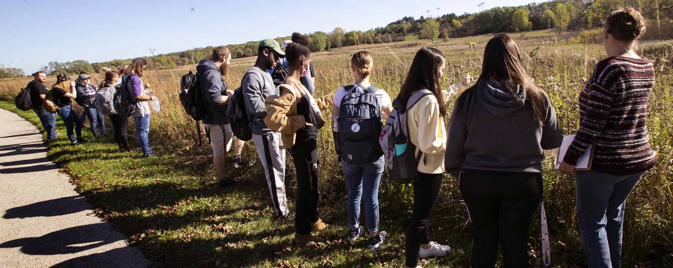 A sociology class stands by a prairie, outdoors.