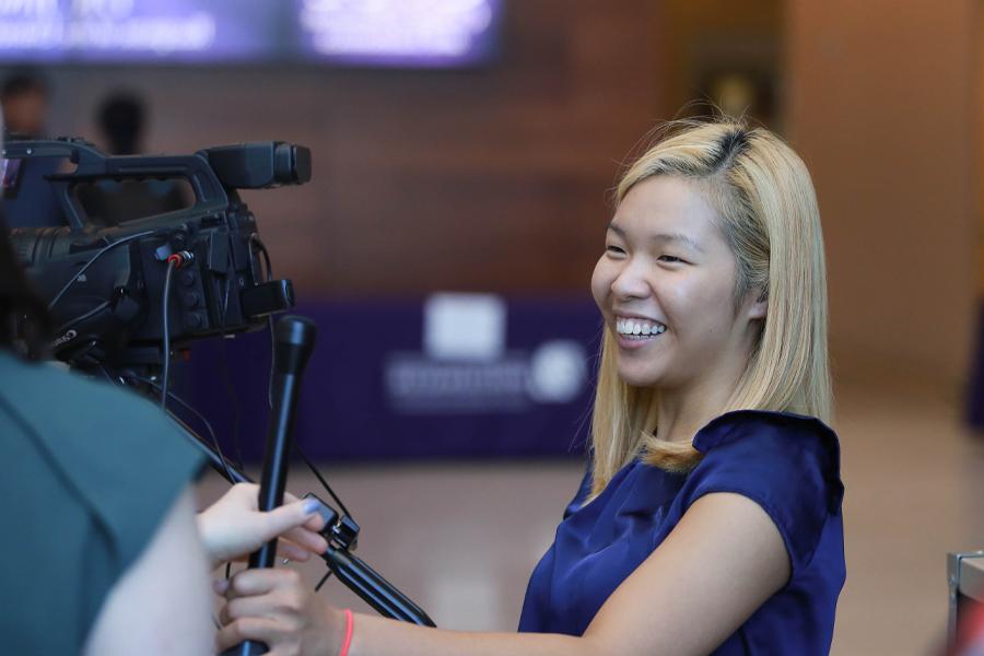 A student smiles while using a video camera.