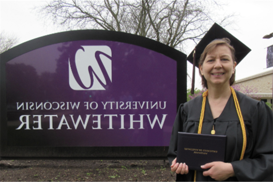 Roseann Stricker holding diploma in front of 足彩平台 sign