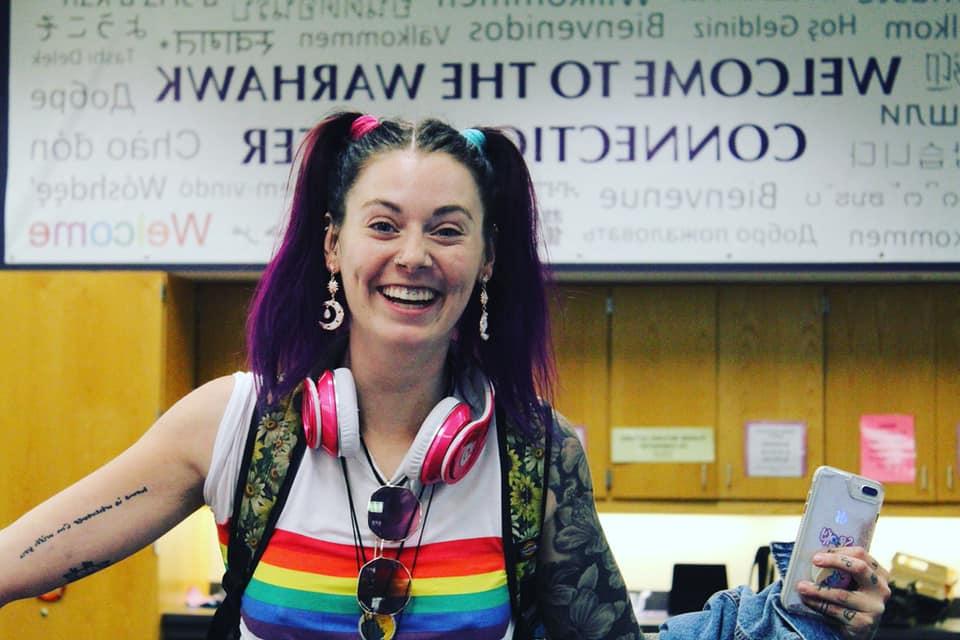 Student smiling in front of the Warhawk Connection Center banner on National Coming Out Day. 