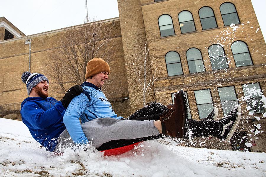 Two people sled down a snowy hill by Hyer Hall.