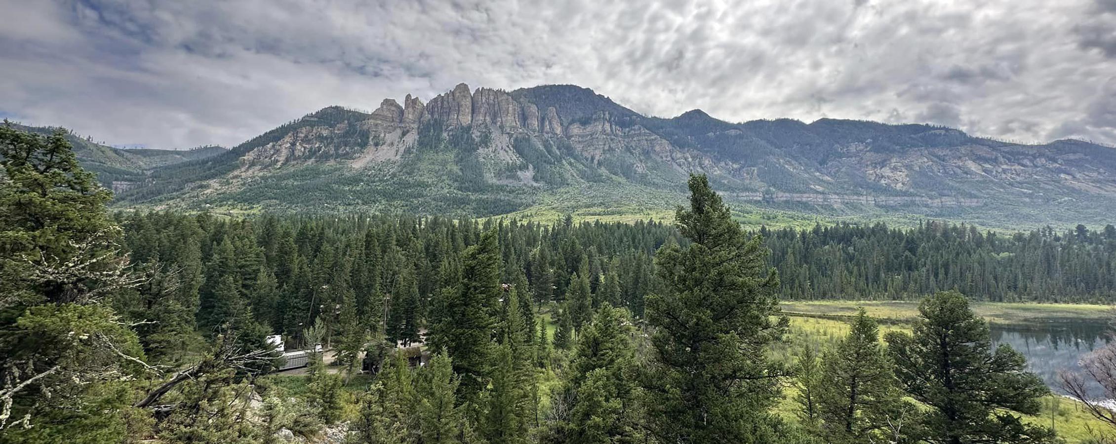 Landscape photo of clouds over a mountain with a forest in the foreground.