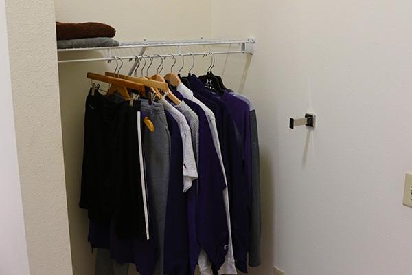 A closet. There is a wire shelf with clothes hanging on it, and a towel rack.