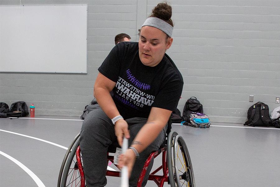 A student in a wheelchair demonstrates a game they have created with a stick and a ball.