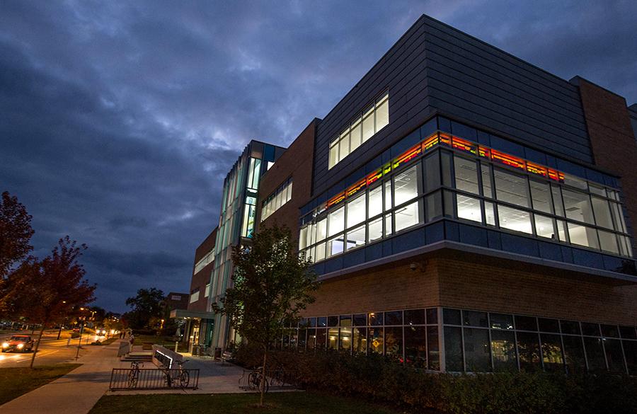 The exterior of Hyland Hall at night with the stock market ticker illuminated through the windows.