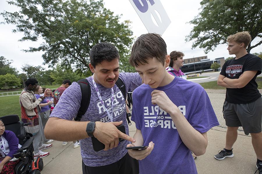 Two students wearing purple shirts stand together during HawkFest.