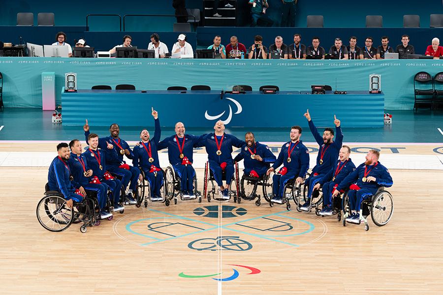 The men's Team USA gathers on the basketball court wearing gold medals.