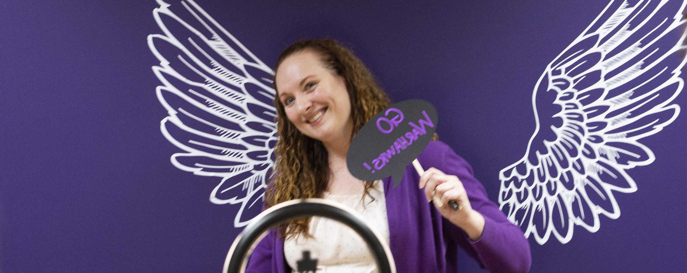 Person stands in front of a purple background with white wings.