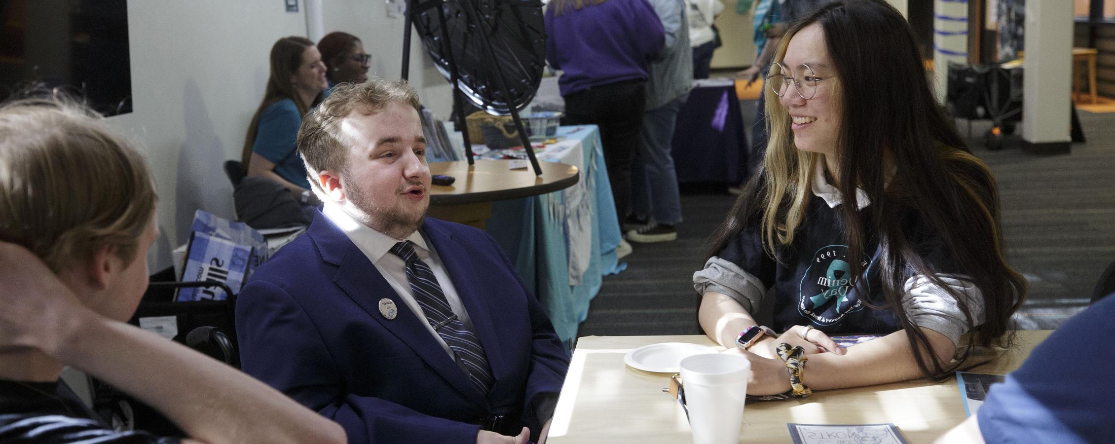 Three students chat together at a tabling event in Fricker Hall.